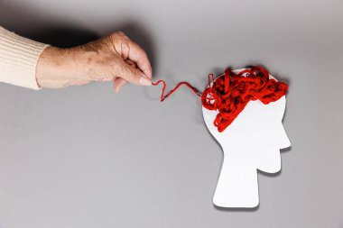 Dünya Alzheimer Günü. Üst sınıftan bir kadının eli kağıt siluetine uzanan kırmızı bir ipliği çeker. Uzayı kopyala Gri arka plan. Psikoloji kavramı.