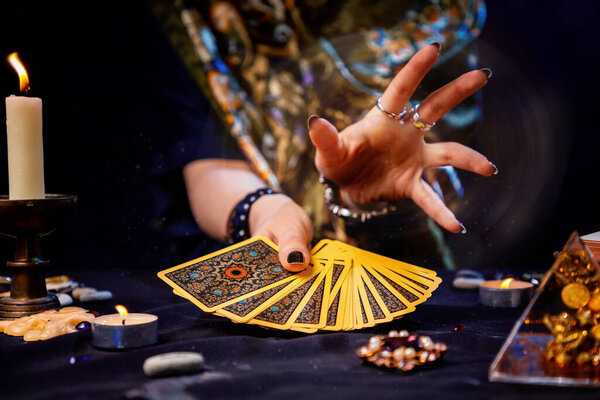 The fortune teller holds a fan of cards in her hands and casts a spell with her hand. Close-up. The concept of divination, magic and esotericism.