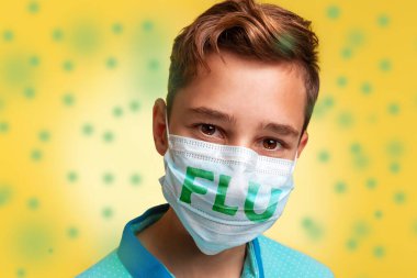 Virüslere ve hastalıklara karşı koruma kavramı. Mavi tişörtlü ve maskeli, üzerinde grip yazan genç bir çocuğun yakın plan portresi. Yeşil bakterili sarı arkaplan.