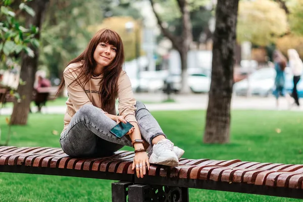 Una Joven Sonriente Está Sentada Banco Con Teléfono Inteligente Sus — Foto de Stock