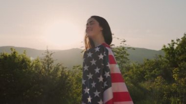 Bağımsızlık Günü. Omzuna Amerikan bayrağı asılmış, gülümseyen beyaz bir kadın, günbatımı gökyüzünün arka planında. Ağır çekim. Dolly vurdu. Vatanseverlik kavramı