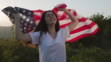 Genç ve güzel bir kadın şarkı söylemeye, dans etmeye ve Amerikan bayrağını sallamaya gider. Günbatımı gökyüzünün arka planında. Ağır çekim. Vatanseverlik kavramı