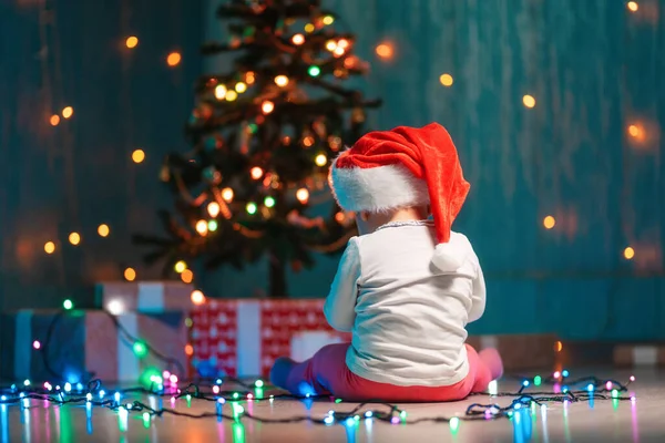 Klein Kind Een Kerstmuts Zittend Met Feestelijke Lichtjes Kerstcadeaus Achteraanzicht — Stockfoto