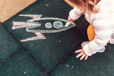 Küçük bir çocuk yere tebeşirli bir roket çiziyor. Üst manzara, yakın plan. Gelecek ve gelişim kavramı.