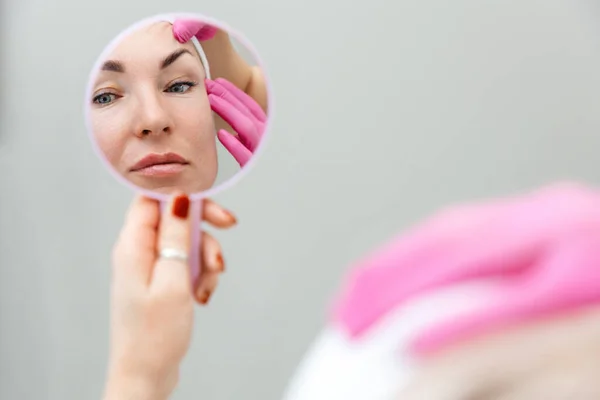 美容整形と美容整形 鏡の中で自分自身を見ている女性の反射 美容師は顧客の眉をすすめる — ストック写真