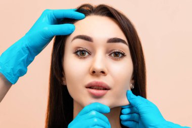 Kozmetik uzmanlarının elleri yüzünün derisini geren güzel bir genç kadının portresi. Masaj ve gençleştirme kavramı.