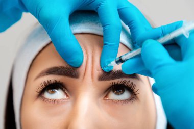 Mavi lastik eldivenli bir doktor hastanın alnındaki kırışıklıklara dolgu yapar. Yakın plan. Profesyonel kozmetoloji ve mezoterapi kavramı.