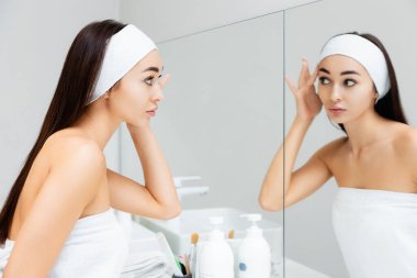 Aynada yüzüne bakan genç ve güzel bir kadının portresi. Profesyonel cilt bakımı ve yaşlanma karşıtı prosedürler.