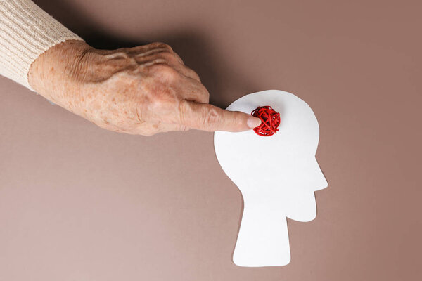Psychology and mental heaslth. The hand of an elderly woman points to a braided red ball in the silhouette of the head. Copy space. Beige background. The concept of psychology.