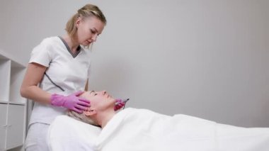 Pembe eldivenli profesyonel güzellik uzmanı müşterinin yüzüne mezoterapi yapıyor. Kozmetik Kliniğinde Yaşlanma Karşıtı Tedavi