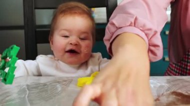 Bir çocuğun yakından çekilmiş portresi gülümseyen ve kurabiye kesiciyle oynayan. Anne hamuru yuvarlıyor. Çocuklarla evde yemek pişirmek.