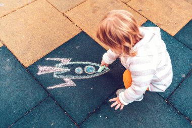 Küçük bir çocuk yere tebeşirli bir roket çiziyor. Üst Manzara. Gelecek ve gelişim kavramı.