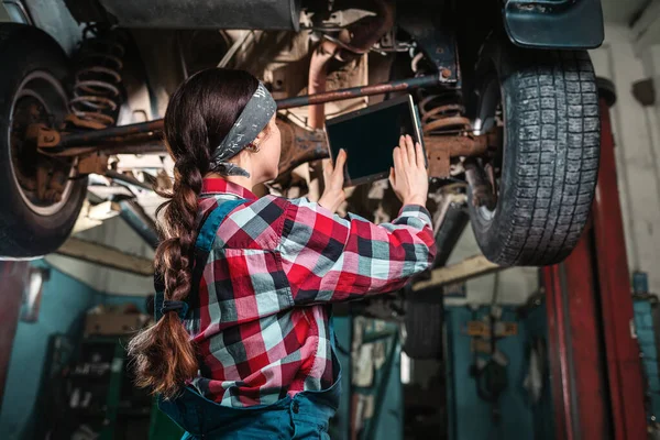 Młoda Mechanik Mundurze Trzyma Tabliczkę Rękach Sprawdza Samochód Samochód Windzie — Zdjęcie stockowe