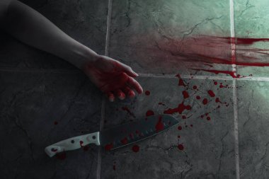Büyük, keskin bir mutfak bıçağı, kanlı bir kadın eli ve kanlı izler. Silah ve kişi yeşil kiremitlerle kaplı yerde yatıyor. Düz yatıyordu. Cinayet ve suç kavramı.