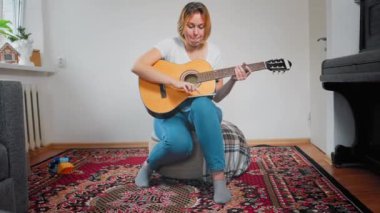 Genç beyaz bir kadın telefonundan online derslerden gitar çalmayı öğreniyor. Hobi ve e-öğrenme kavramı.