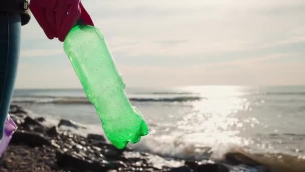Vapaaehtoinen Kumihansikkaissa Pitää Muovipulloa Laittaa Sen Roskapussiin Meri Taustalla Ympäristönsuojelun — kuvapankkivideo