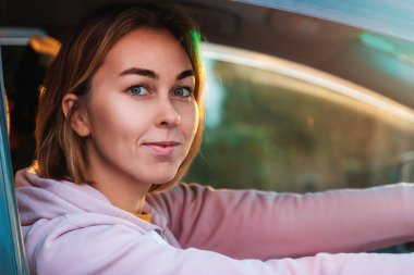 Sağlak bir arabanın direksiyonunda oturan gülümseyen, kendinden emin genç bir kadının portresi. Araba kullanmayı öğrenmek ve ehliyet almak..