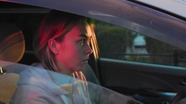 A young Caucasian woman is sitting behind the wheel of a car and nervously looks in the rearview mirror, waiting for a policeman. The police siren light is blinking.