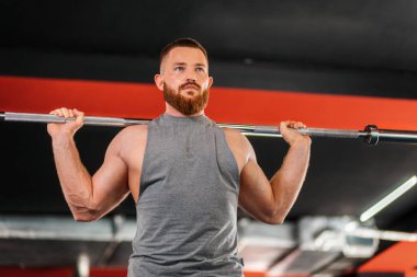A young bearded athletic man trains in the gym, lifting a barbell. Bottom view. The concept of fitness and training.