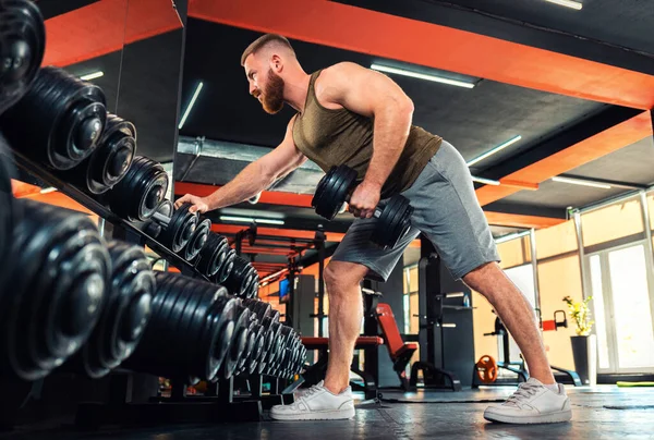 A young bearded athletic man with effort trains with dumbbells in the gym. Bent over row. Bottom view. The concept of fitness.