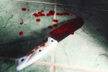 Close up view of big sharp knife with blood. Weapon lies at on the floor lined with green tiles. Copy space. The concept of violence, crime and murder.