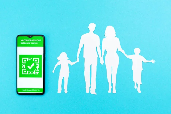 予防接種の概念と新しい通常 デジタル免疫パスポートのアプリと青い背景に紙から切り取られた家族のシルエットと携帯電話 — ストック写真