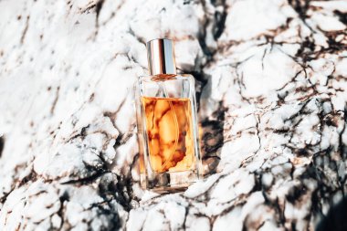 Perfumery. A glass transparent bottle of golden perfume standing on a white marble stone. Top view.