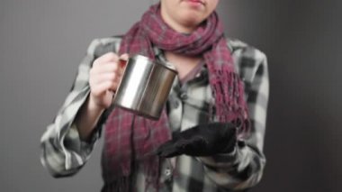 A homeless woman pours coins out of a steel cup and counts them with sadness. Close-up, studio shot. The concept of helping the vagabonds.