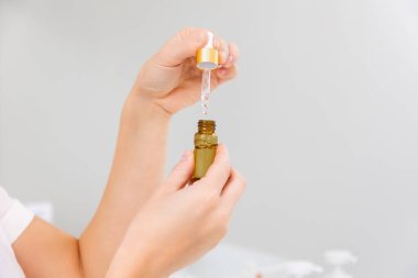 Female's hands hold a small bottle of cosmetic oil or serum. Close-up. Gray background. Copy space. Skin care concept.