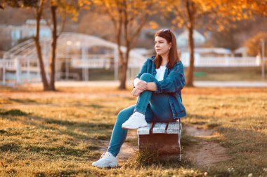 A young woman is sitting on a bench in an autumn park. The concept of loneliness and psychology.