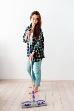 The concept of cleaning. Young pretty woman in casual clothes washing floors. There is a white wall in the background. There's a clean cleaning trail on the floor.