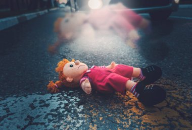 A sad plush doll is lying on the road at a pedestrian crossing. The soul flies out of the toy. There is a car in the background. The concept of a traffic accident.