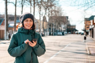 Social network. A young smiling caucasian woman uses a smartphone on the street. Outdoor. Concept of of modern technology.