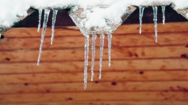 Çatının saçağında asılı duran keskin buz saçaklarının alt görüntüsü yavaşça eriyor. Bahar damlaları.
