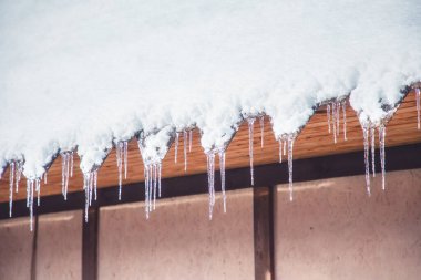 Keskin buz saçakları ve erimiş kar çatıdan sarkıyor. Baharın başında eriyen buzlar.