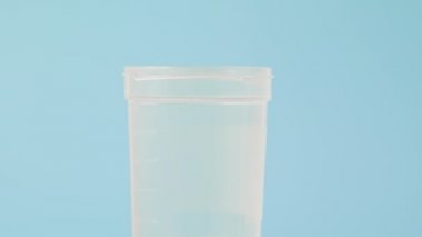 Analiz için plastik bir kavanoza yakın çekim. Sperm örneği incelenmek üzere yerleştiriliyor. Mavi arka plan. Sperm bağışı ve iktidarsızlık kavramı..