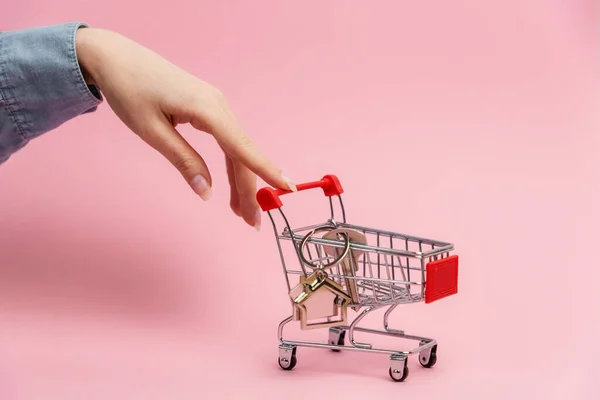 女店员推着装有钥匙和家庭钥匙链的购物车 粉色背景 房地产租赁和抵押的概念 — 图库照片