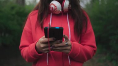 Genç bir kadın düşünceli bir şekilde kulaklıklı bir telefona yazı yazıyor. Jib çekimi