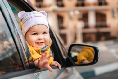 Şapkalı, kulaklı, camdan dışarı bakıp el sallayan beyaz bir çocuğun portresi..