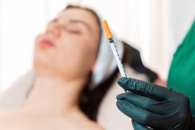 Beaitician 'ın elinde yenilenme işlemi için enjeksiyon yapılmış bir şırınga var. Kuaförde mezoterapi. Arka planda odaklı olmayan istemci.
