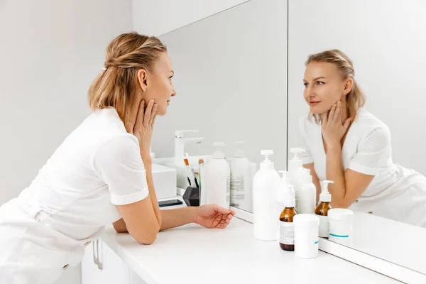 鏡を見た若い美少女は 自分に微笑む 鏡の近くに立って化粧品ボトル スキンケアコンセプト — ストック写真