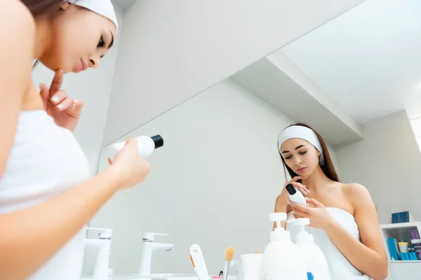 化粧品のボトルを持ち 製品の組成物を読んでいる若い女性は バスルームに立っています 一番下だ スキンケアの概念 — ストック写真