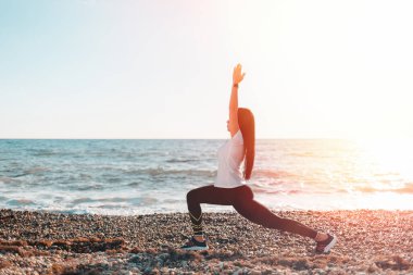 Yoga ve açık hava sporları konsepti. Kayalık bir plajda yoga yapan genç bir kadın. Boşluk ve ışığı kopyala.