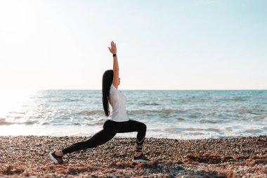 Yoga ve açık hava sporları konsepti. Kayalık bir plajda yoga yapan genç bir kadın. Boşluğu kopyala.