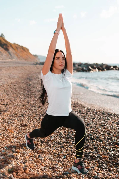 The concept of yoga and outdoor sports. A young woman doing yoga on a rocky beach. Front view. Vertical orientation.