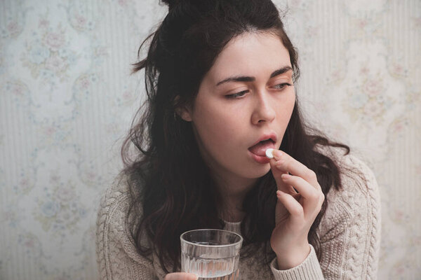 Молодая девушка принимает аспирин от головной боли.