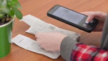 Bir kadın satın alma makbuzlarına bakar ve telefonuyla fotoğraflarını çeker. Eller yakın çekim. Ev Muhasebe ve Yatırımları.