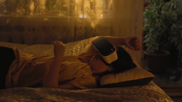 一个年轻的女人躺在床上 摘下她的虚拟现实眼镜 疲倦地擦拭着她的眼睛 家庭中的娱乐活动 — 图库视频影像