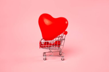 Sevgililer Günü. Üzerinde pembe arka planda kalp şeklinde bir balon olan mini alışveriş arabası. Tatil alışverişi kavramı.