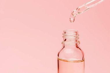 Şeffaf cam bir şişeye serumla ve bir damla pipetle yakından bak. Fotokopi alanı ile pembe arkaplan. Güzellik ürünleri konsepti.